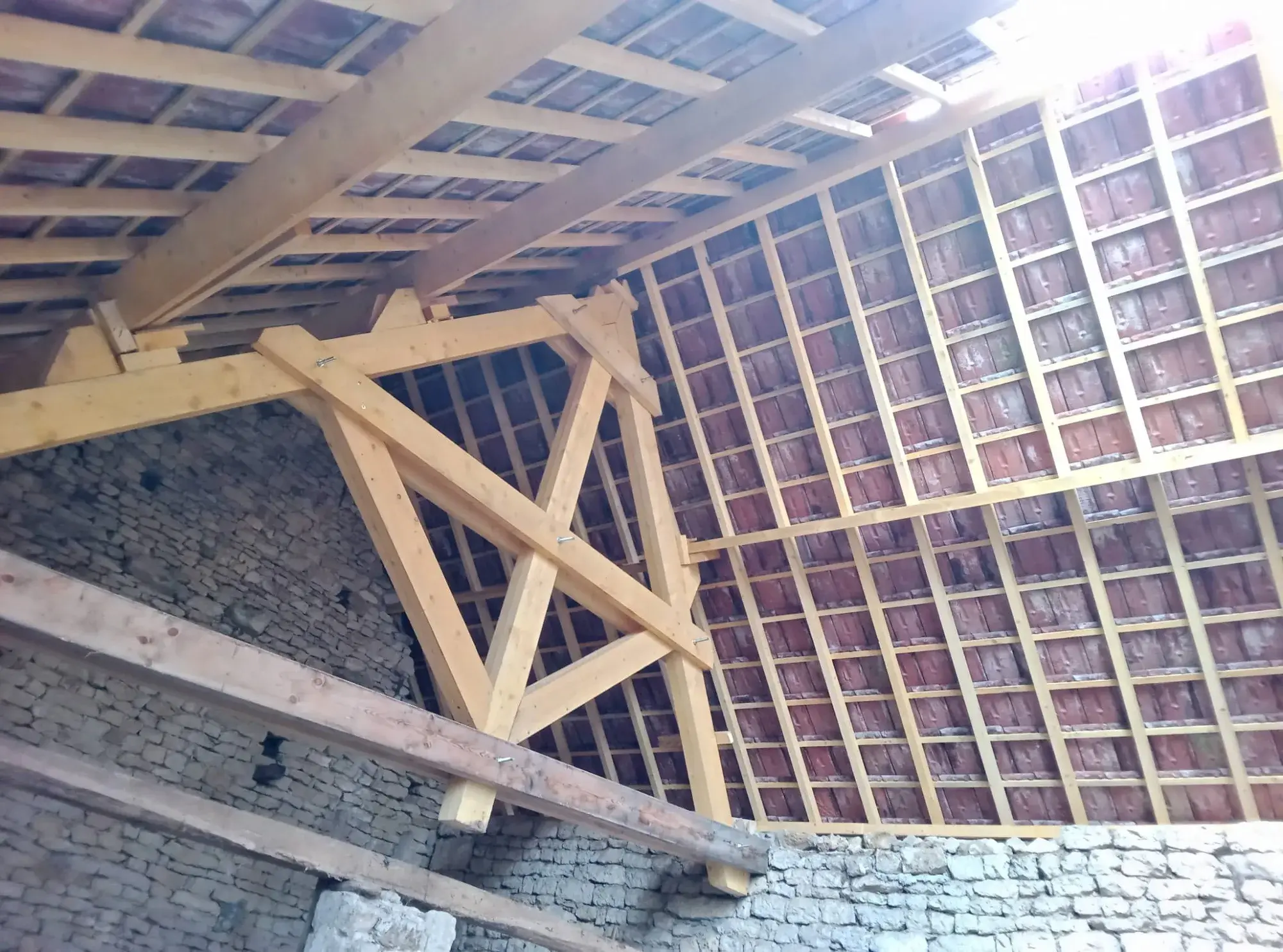 Charpente traditionnelle en sapin vue de l’intérieur, liteaux réguliers et tuiles neuves posées