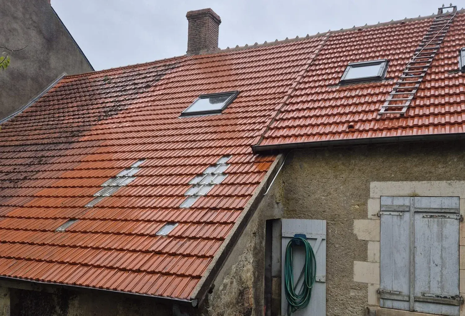 Toiture de longère en cours de démoussage : la partie haute encore noircie de mousse