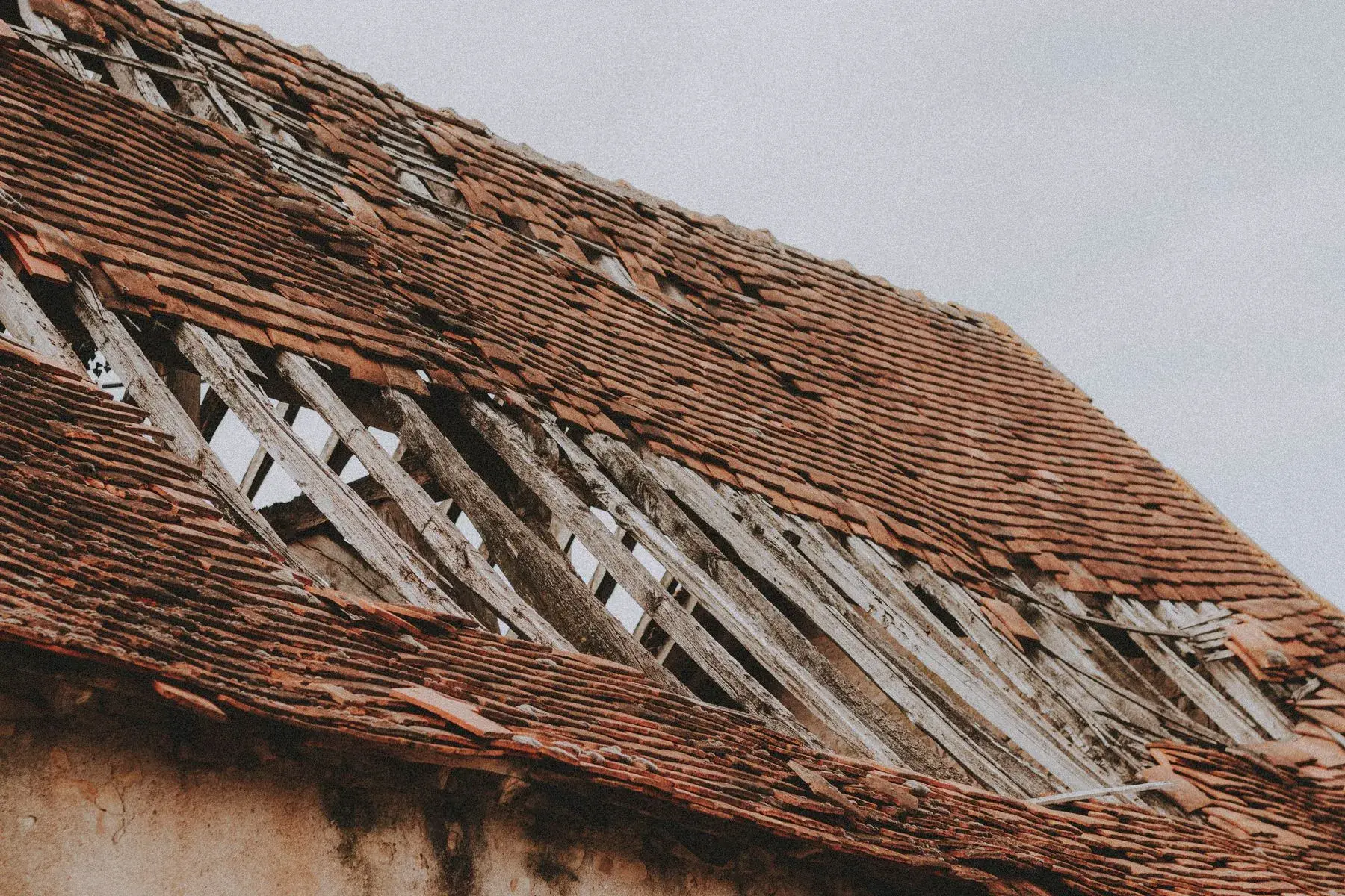 Toiture ancienne effondrée par endroits, tuiles manquantes et liteaux à nu